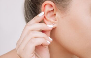 Ear piercing. Cropped shot of a young woman wearing elegant stud earrings on a gray background. Jewelry with gemstones, accessories